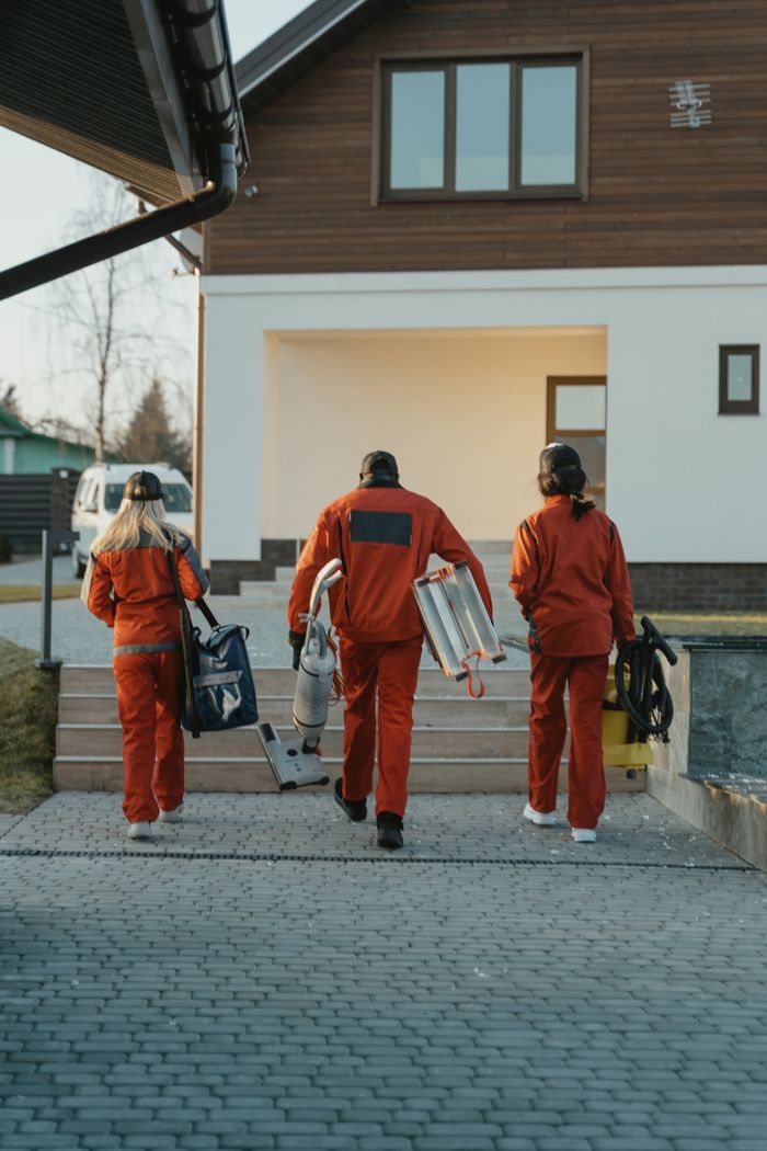 about-us-02 Équipe de nettoyage en uniformes rouges avec leur matériel s’approchant de l’extérieur d’une maison moderne.